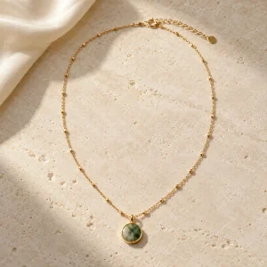 Concept illustration: fine gold tone necklace arranged in an elegant oval with one small round green and ivory balanced pendant. Not an actual product photograph.