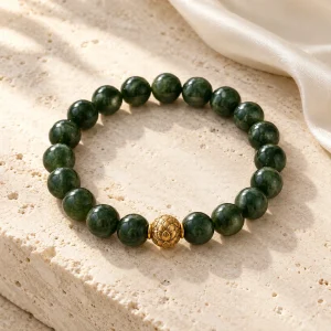 Concept illustration: dark green bead bracelet with one warm gold tone accent, awakening inspired. Not an actual product photograph.